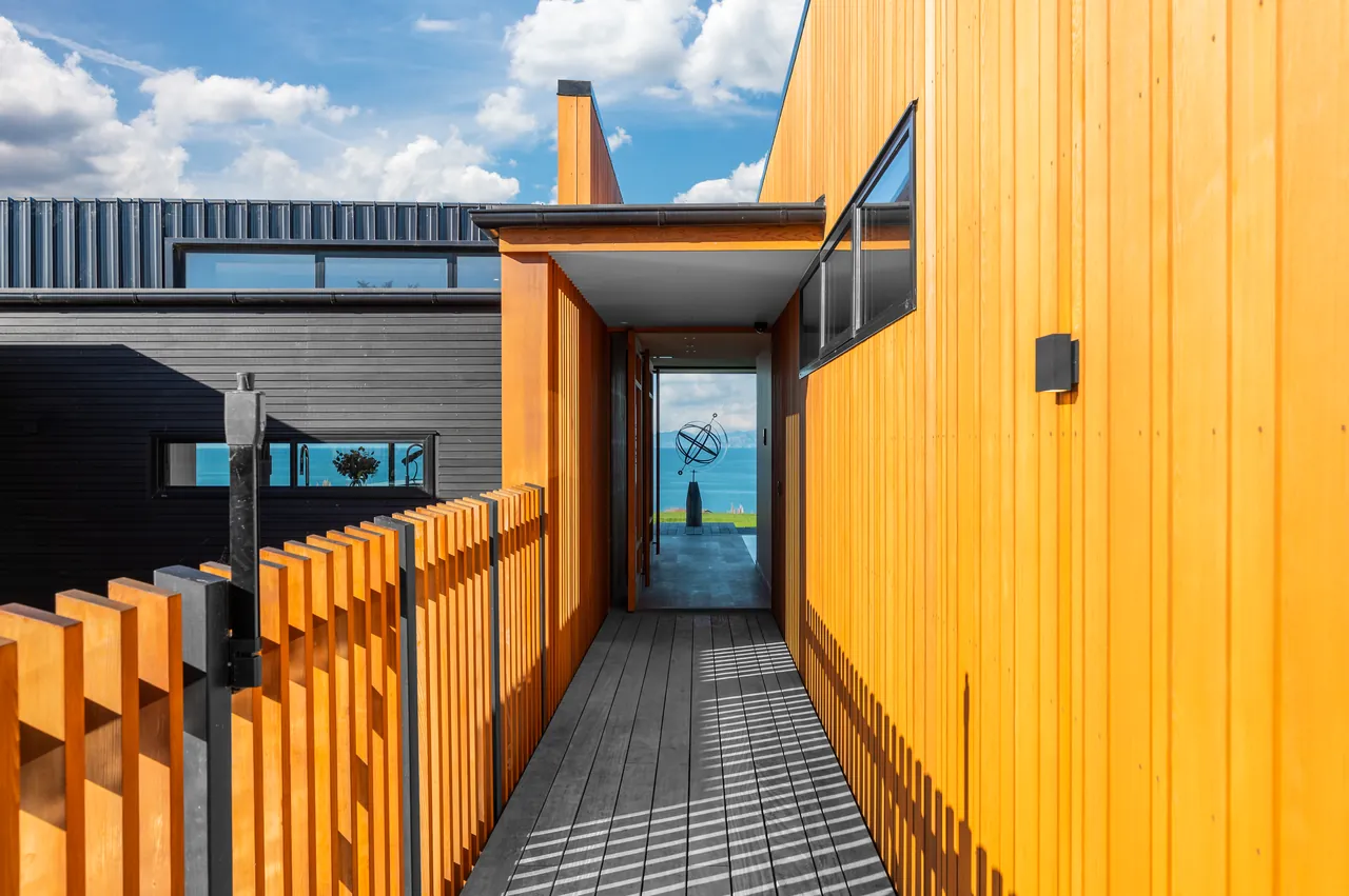 Cedar-clad entry walkway with a slatted fence, framing a glimpse of the sea