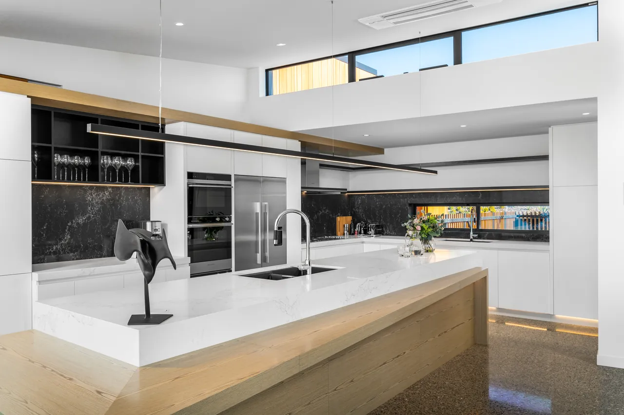Gourmet kitchen with a white stone island, black marble splashback and double oven